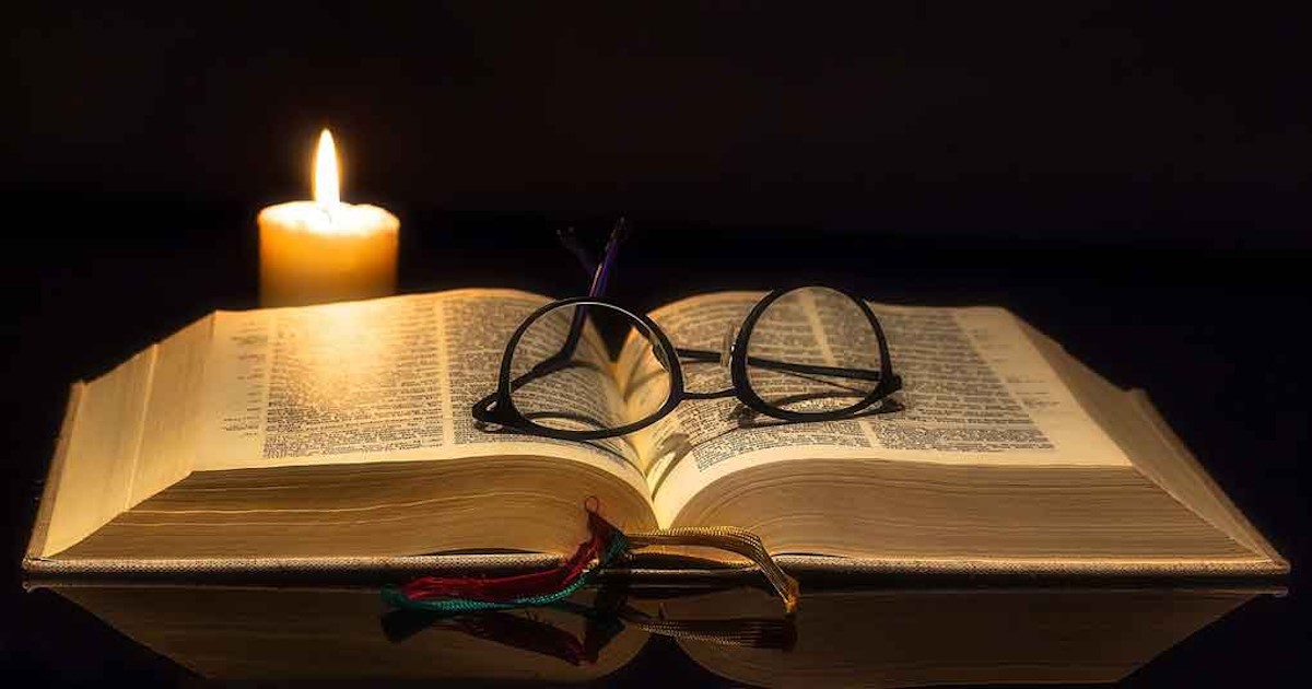 Open Bible with a pair of glasses and candle.